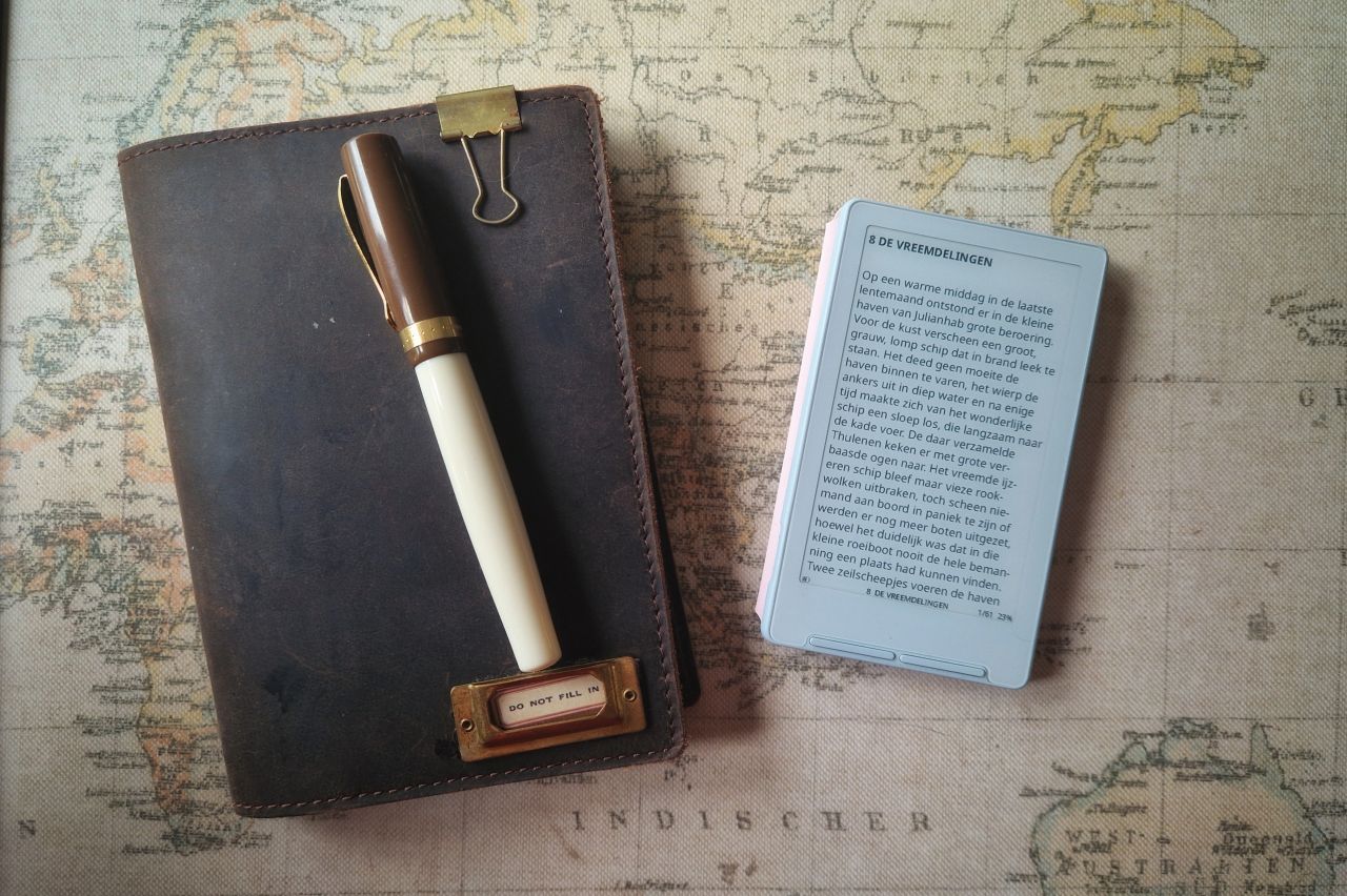 The XTEink X4 e-reader alongside a leather journal and fountain pen on a vintage map