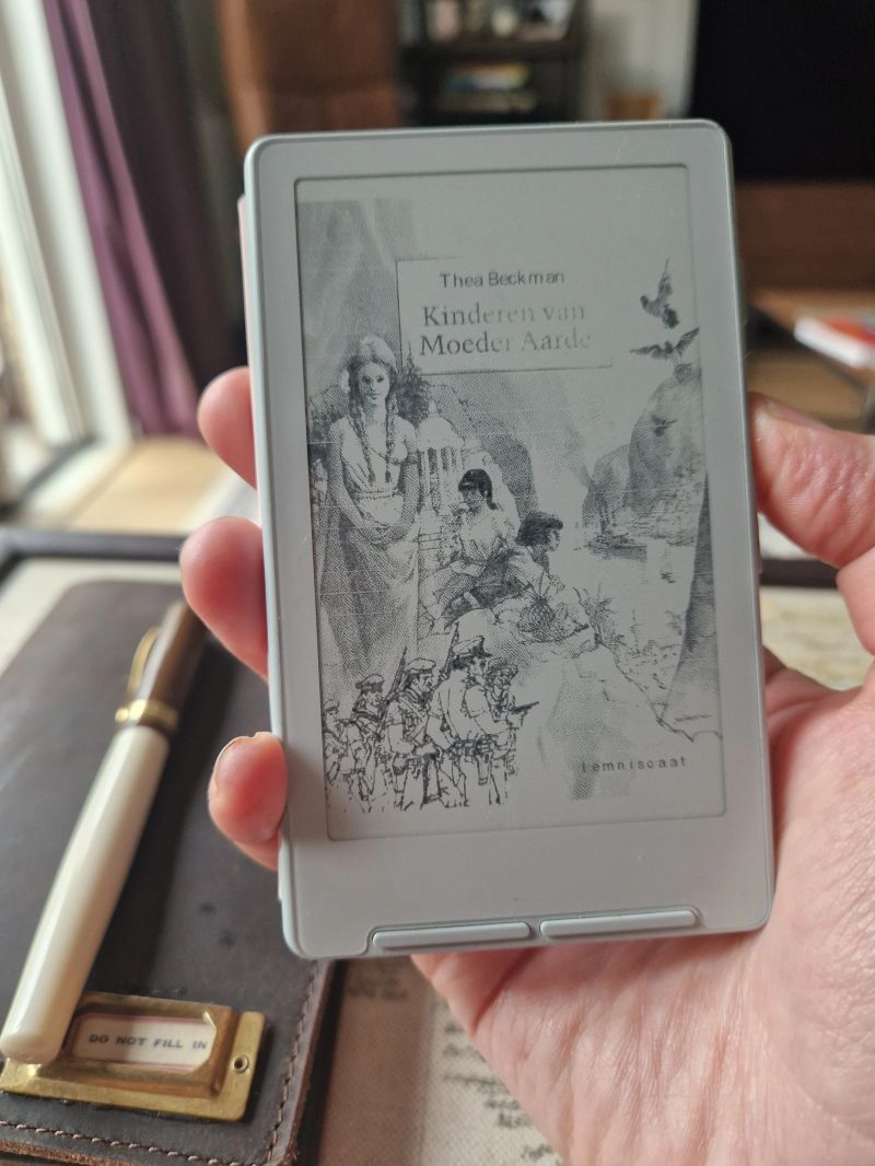 Holding the e-reader showing Kinderen van Moeder Aarde by Thea Beckman — the device fits in one hand